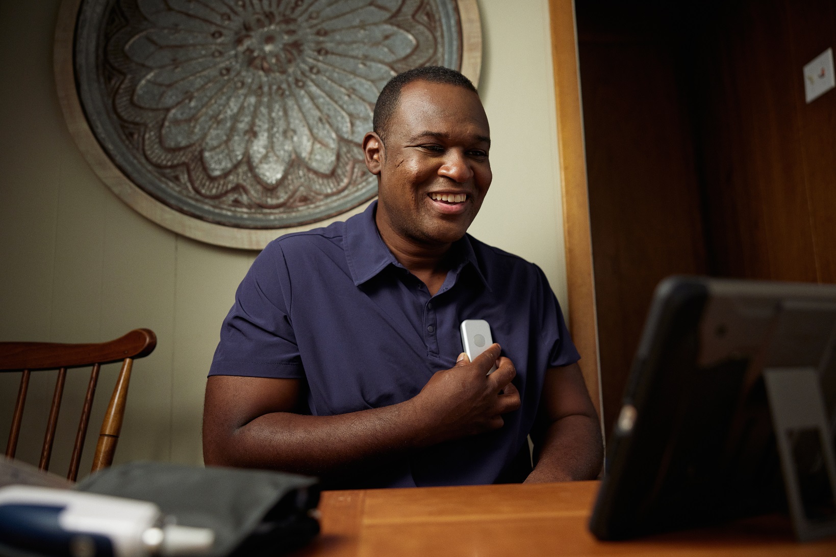 African American man in blue shirt holds remote monitoring device to his chest