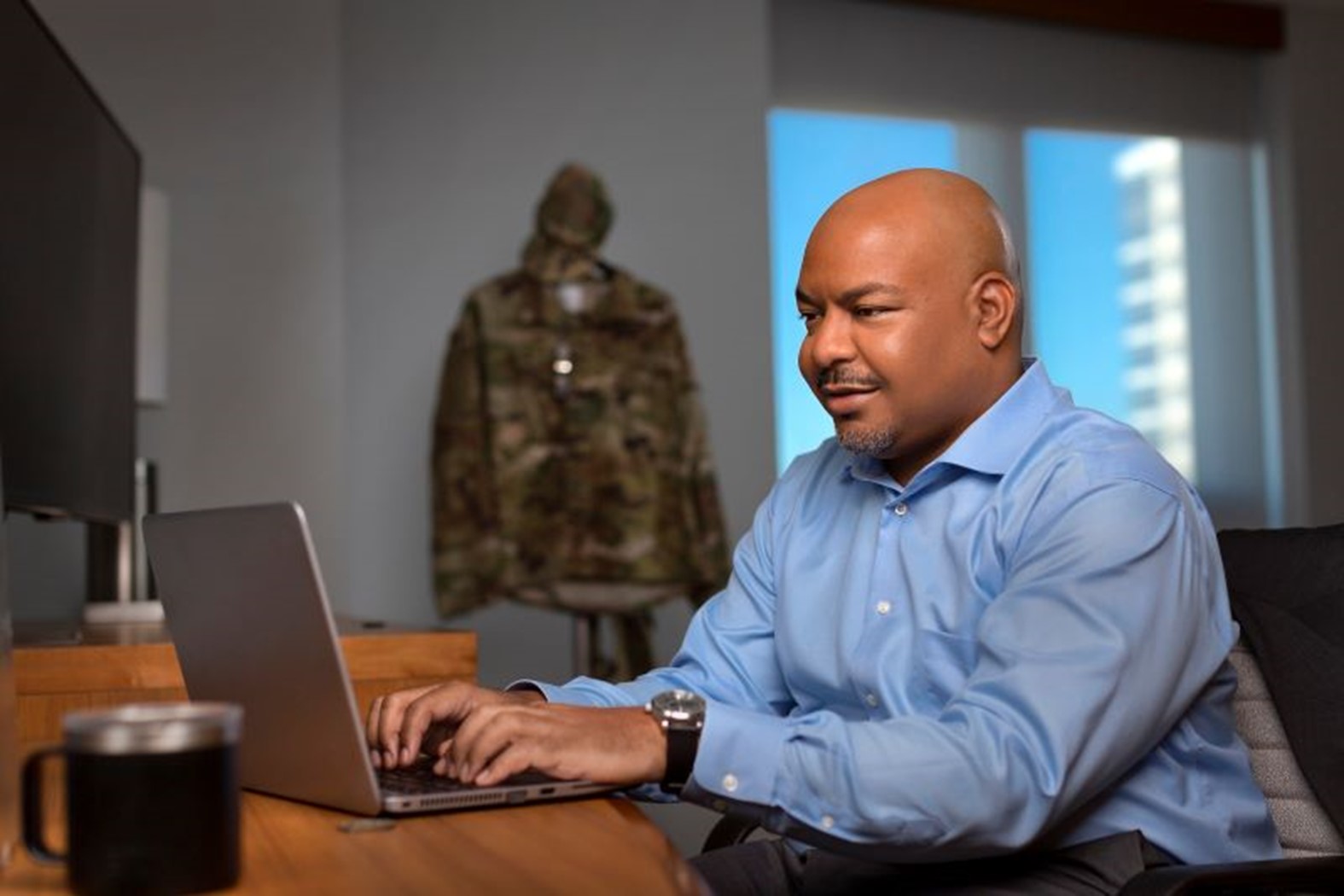 Black man in light blue shirt sits with a laptop in front of him