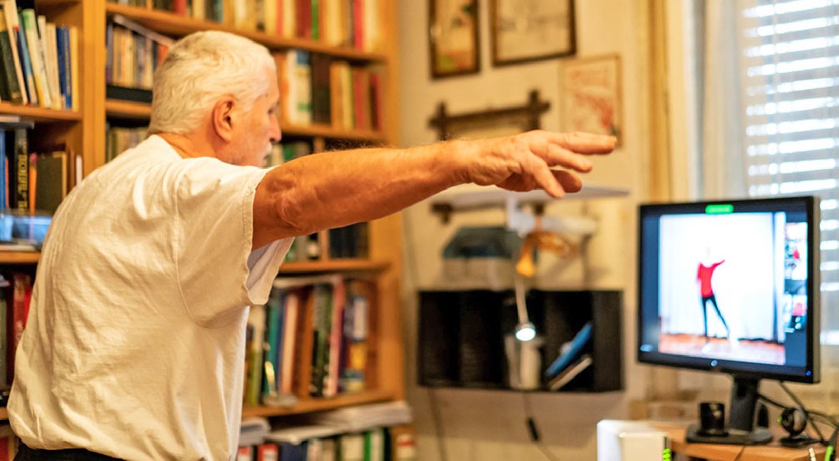 older man stretches in front of a computer monitor 