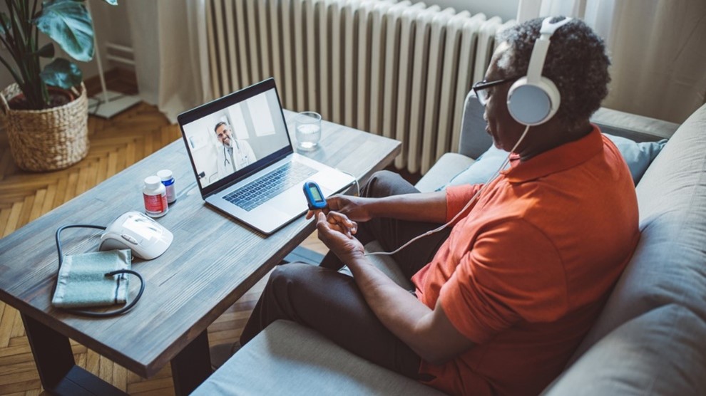 Black Veteran wears headphones and uses remote monitoring device while on a video visit with a doctor