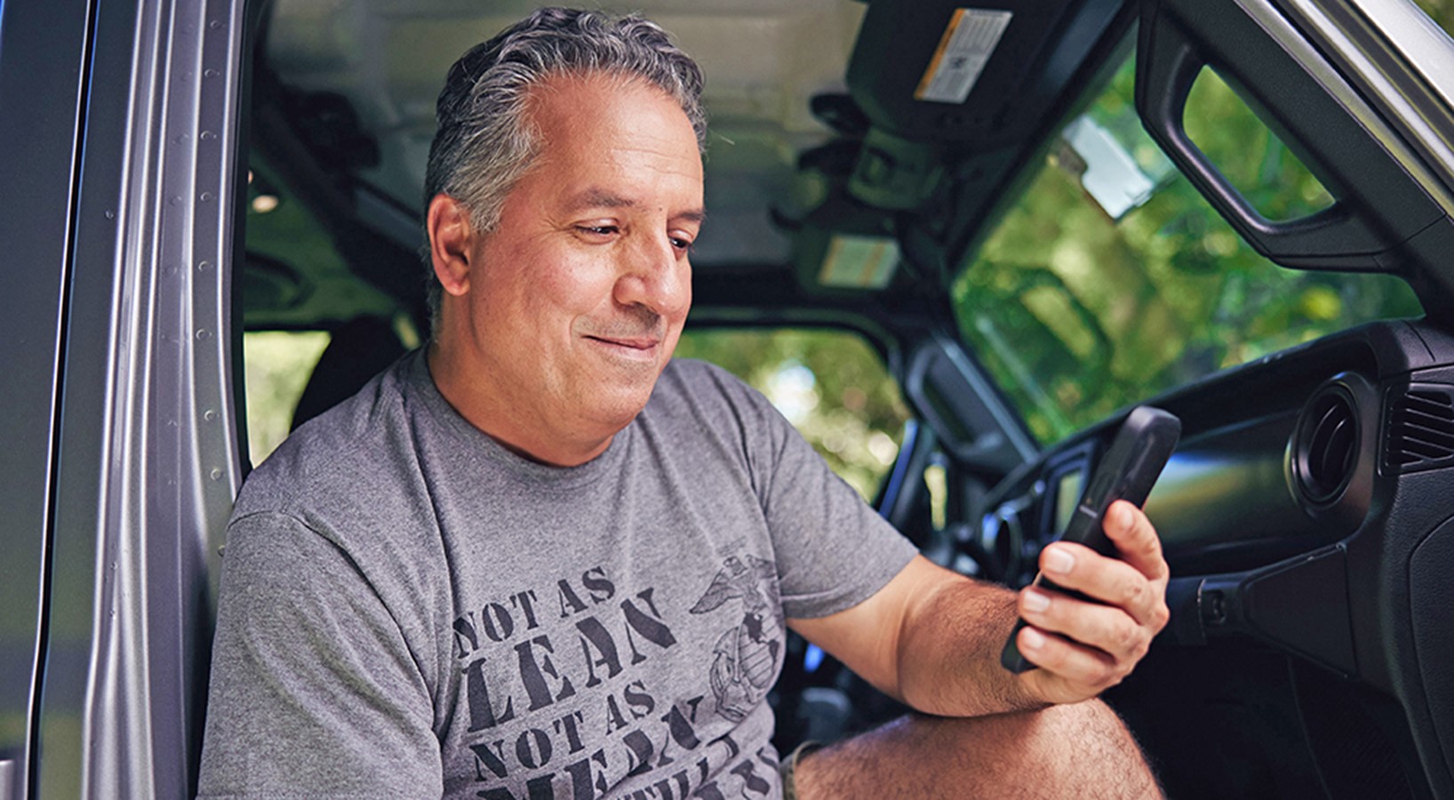 middle aged man holds and looks at his phone while sitting in his car