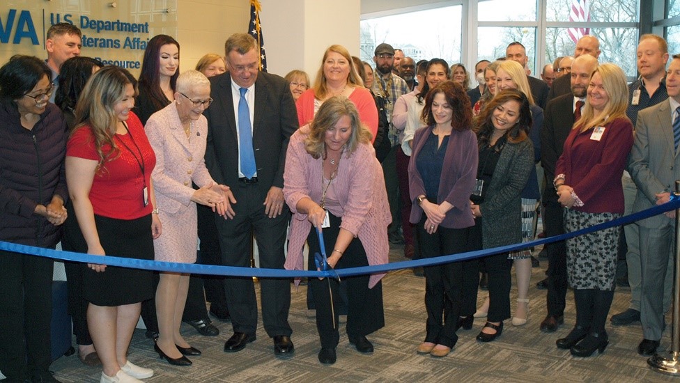 Woman in pink sweater cuts ceremonial ribbon surrounded by other people