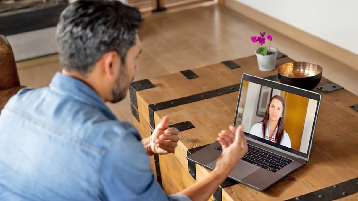 man sits in front of computer screen and talks to a female provider by video