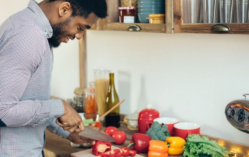 Young Black man cuts colorful vegetables on cutting board