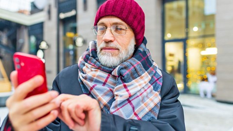 Veteran wearing a beanie and scarf checking his smartphone outside. 