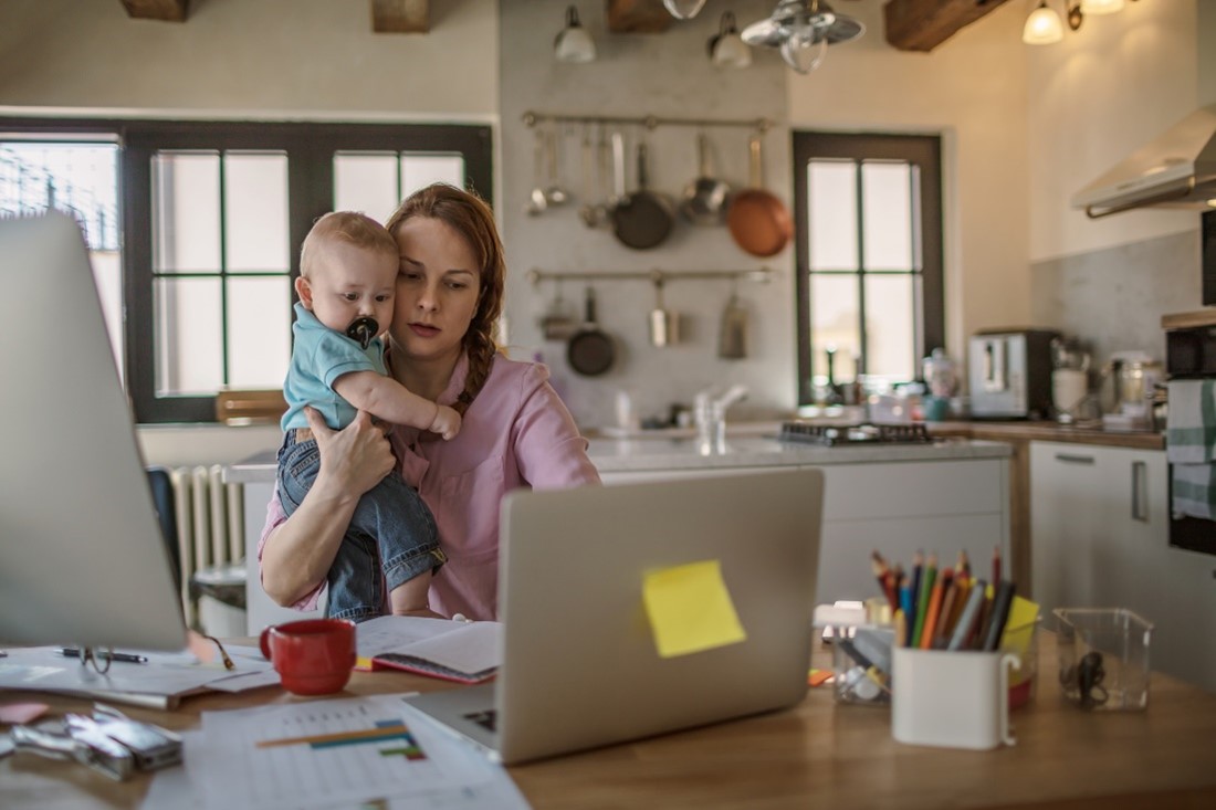 A woman holding her baby while looking at a laptop.