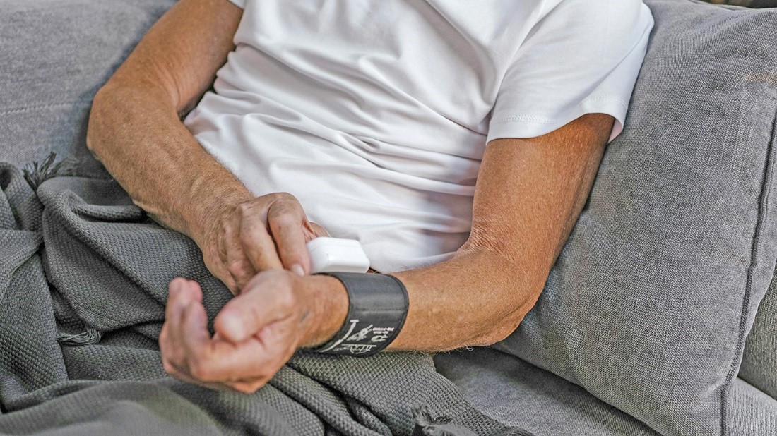 A Veteran using a blood pressure cuff while sitting on a couch. 