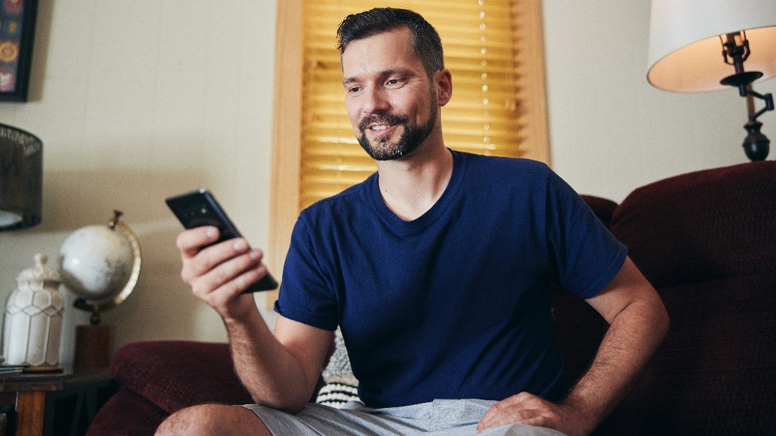 A man sitting on the couch and looking at his smartphone.