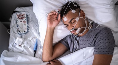 A man sleeping with medical equipment taped to him.