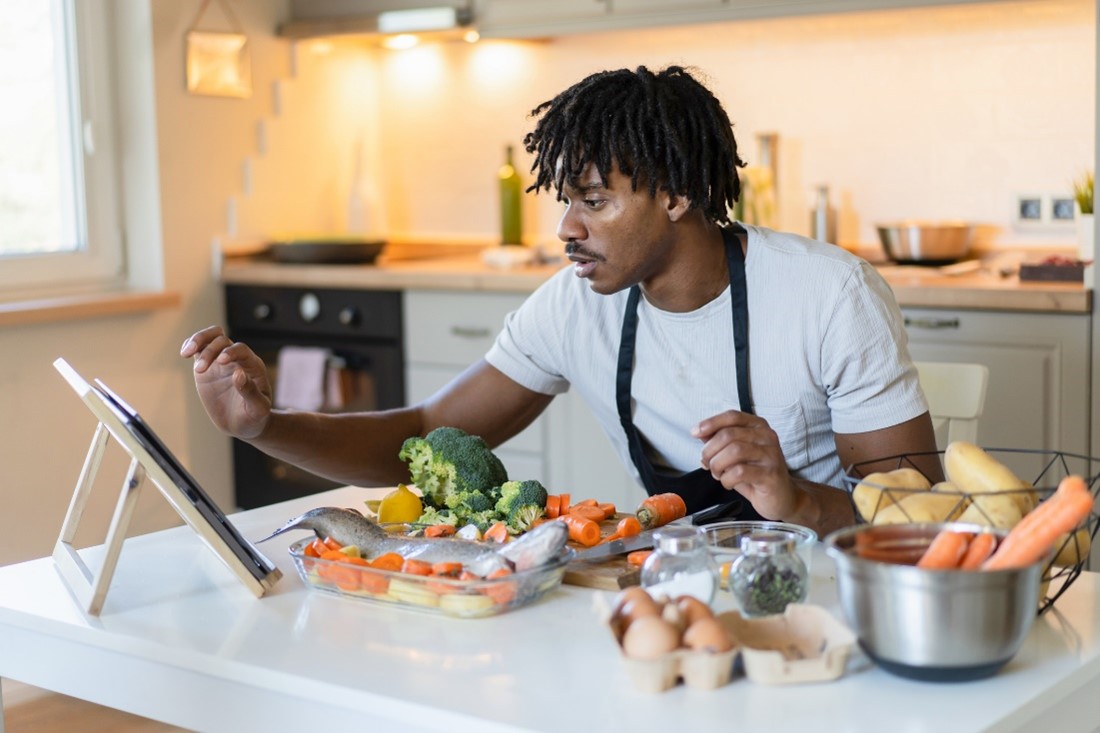 A man looking at his tablet while cooking. 