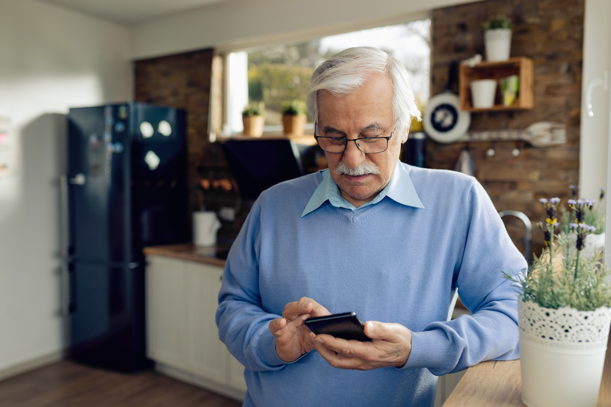 Older man wearing a light blue sweater types on cell phone 