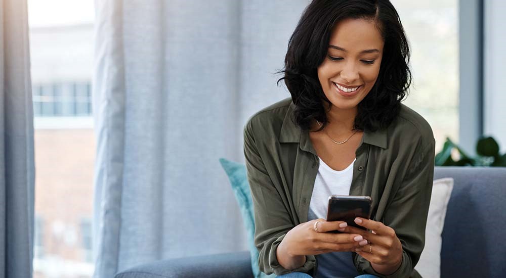 Woman smiles while holding and looking at her mobile device