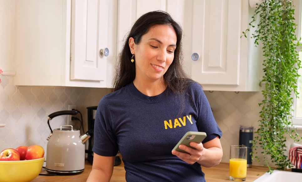 A woman wearing a U.S. navy shirt checking her smart phone.