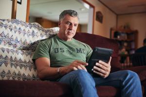 Man in green shirt sits on coach and looks at tablet