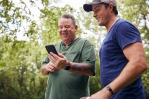 Older man and younger man look at phone together outside