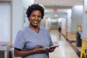 Black woman in scrubs holds tablet and smiles