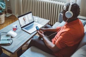 Black Veteran wears headphones and uses remote monitoring device while on a video visit with a doctor