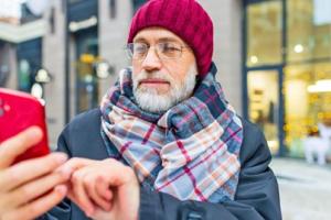 Veteran wearing a beanie and scarf checking his smartphone outside. 