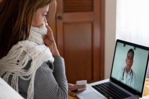 Woman in scarf sits in front of computer with provider on video.