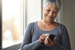 Woman with grey hair texting on a smartphone and smiling 
