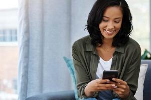 Woman smiles while holding and looking at her mobile device