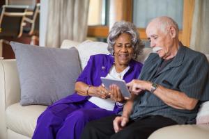 man and woman sit next to each other on couch and look at tablet
