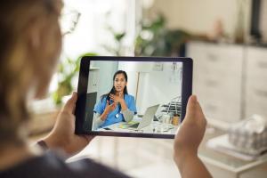 woman provider wearing blue scrubs on-screen of an tablet videoconferences with woman holding the tablet