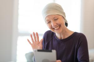 White woman with head wrap hold tablet, smiles, and waves