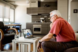 Older White man sits on couch and talks to provider on the computer by video
