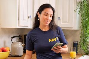 A woman wearing a U.S. navy shirt checking her smart phone.