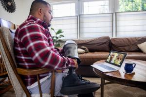 Middle-aged man holds his injured leg and visits with his providers by video on his computer