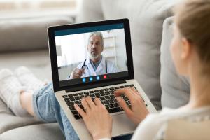 young White woman sits down on couch and videoconferences with doctor via a laptop