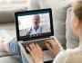 young White woman sits down on couch and videoconferences with doctor via a laptop