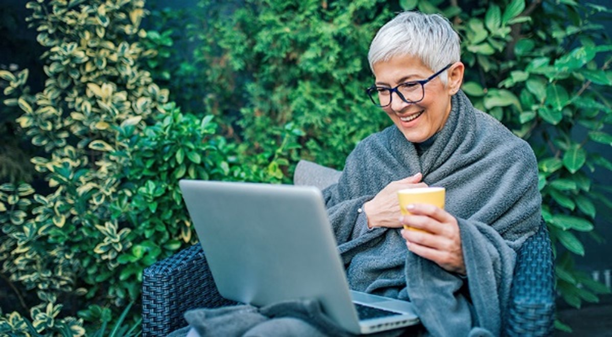 woman with white hair sits in front of a laptop outside