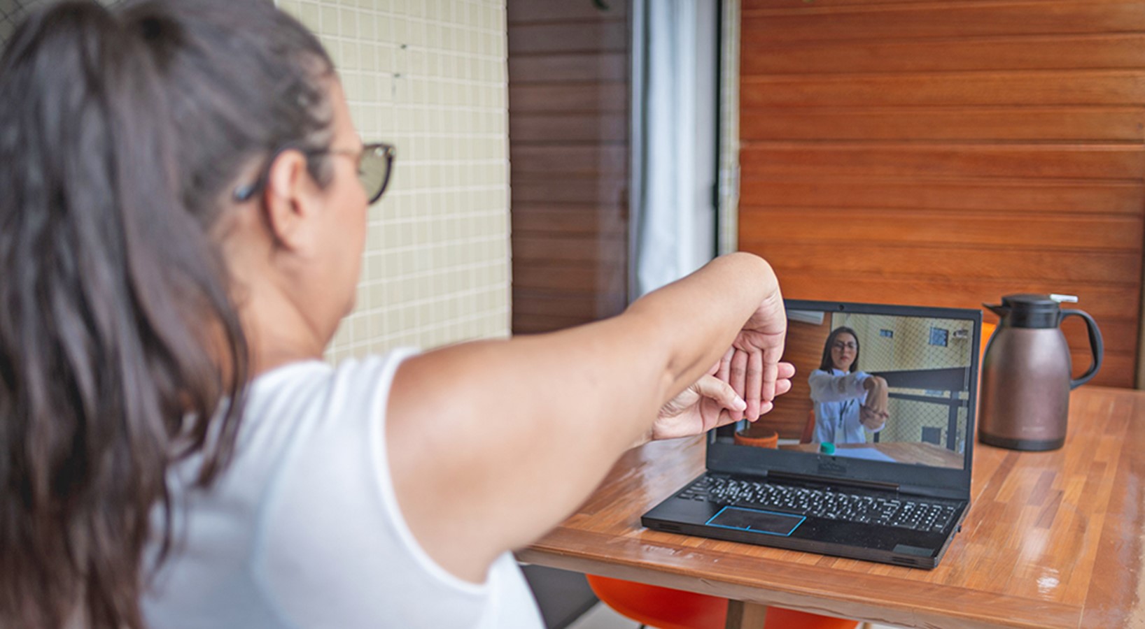 woman with brown hair stretches wrist in front of computer with provider on video