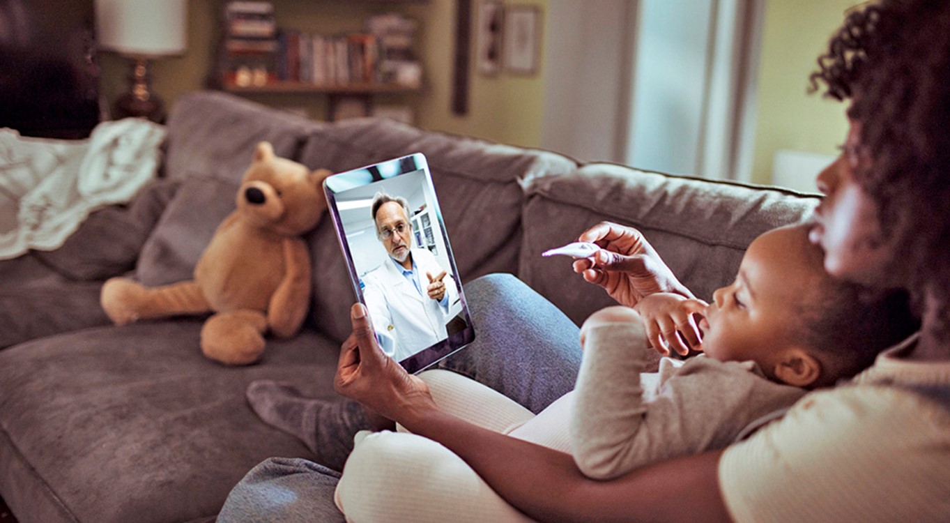 Black woman sits with a child between her arms as they video conference with a health care provider