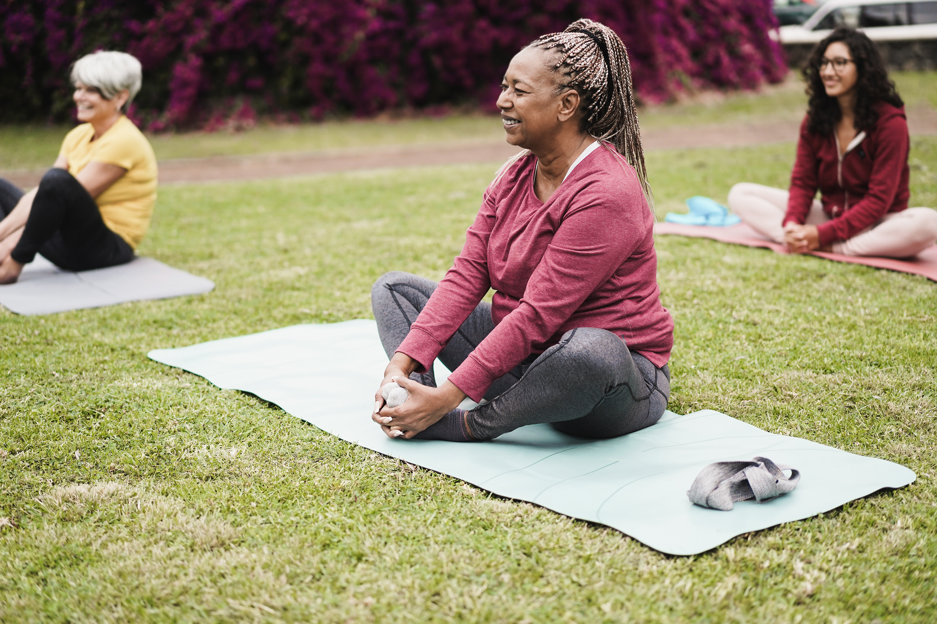 Black woman sits on yoga mat on the grass with her feet together