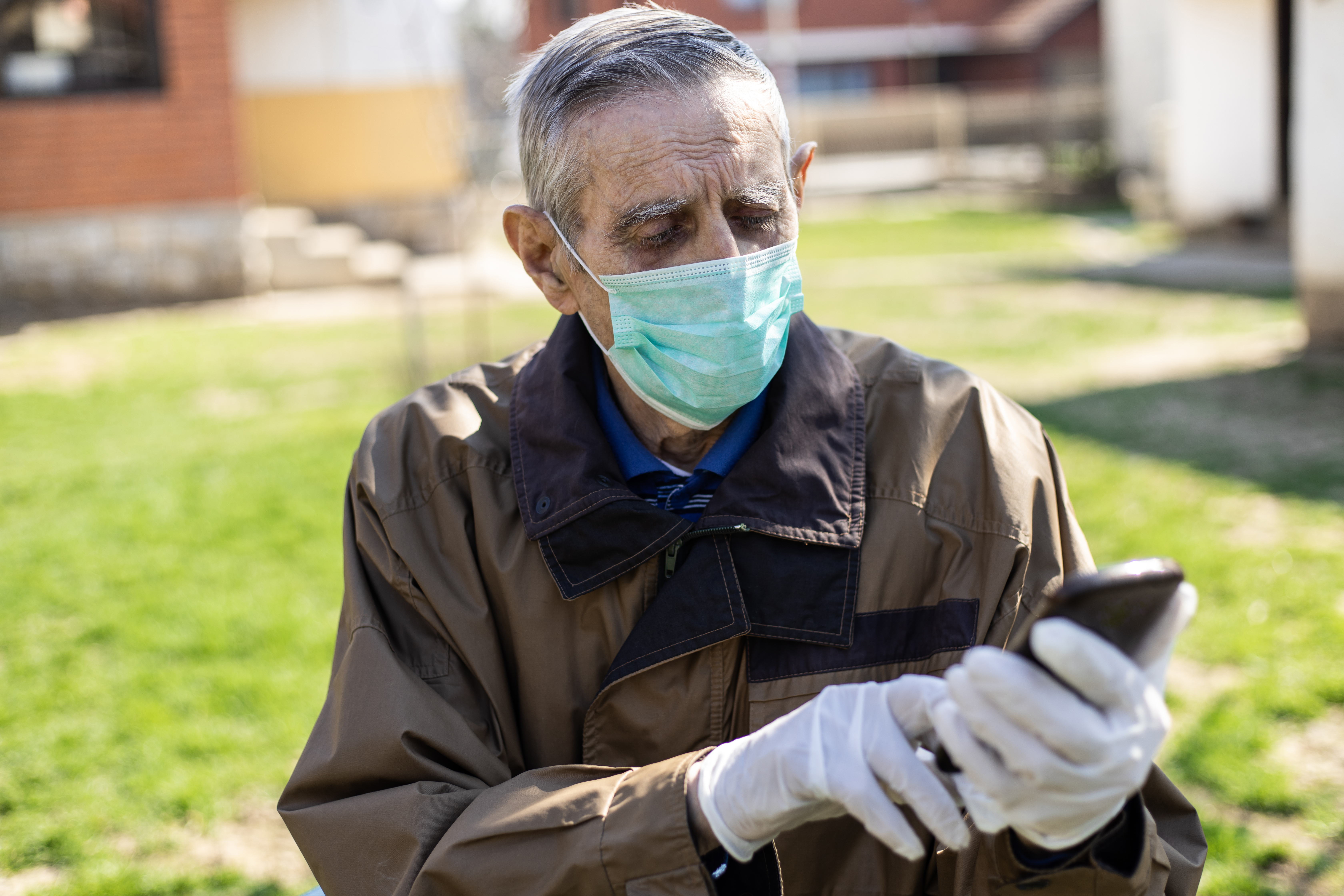 Elderly man in brown jacket and mask holds phone 