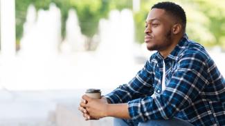 Black man holds coffee and looks into distance